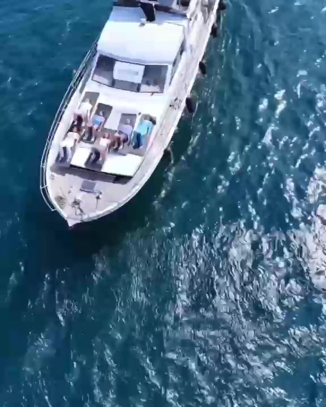Mavi denizde ilerleyen beyaz bir teknenin yukarıdan görüntüsü.