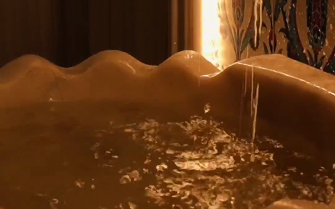 Qualia Spa hamamında altın tonlu mermer kurnaya akan su.